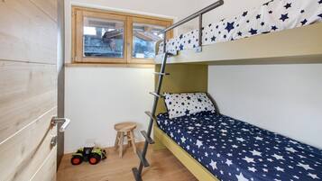 Ein Stockbett mit Bettdecke mit Sternenmuster, eine Holzleiter, ein Fenster mit Blick und ein kleiner Hocker mit einem Spielzeugtraktor.