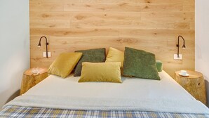 A bed with a wooden headboard, multiple pillows, bedside tables with lamps, and a plaid blanket. - Apartment "Violet a due passi da Bormio" with Mountain View, Private Balcony & Wi-Fi (Valdidentro)
