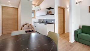 A modern kitchen with a built-in oven, a dining table, and a green sofa in a bright room with wooden beams. - Apartment "Violet a due passi da Bormio" with Mountain View, Private Balcony & Wi-Fi (Valdidentro)