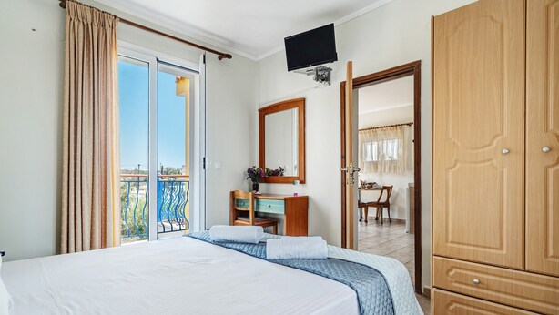 A hotel room with a bed, a desk, a mirror, a wardrobe, and a balcony with a view.