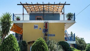 A two-story building with a balcony, a pergola, and potted plants.