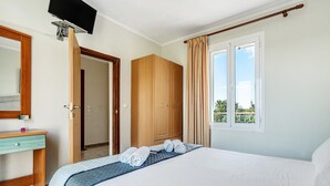 A hotel room with a bed, a desk, a wardrobe, a television mounted on the wall, and a window with curtains.