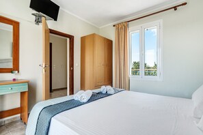 Une chambre d’hôtel comprenant un lit, un bureau, une armoire, un téléviseur fixé au mur et une fenêtre avec des rideaux.
