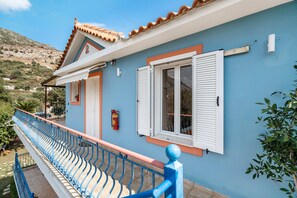 A blue building with white shutters, a balcony with blue railings, and a fire extinguisher mounted on the wall.