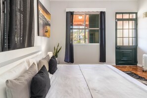 A bedroom with a bed, a window with curtains, a door, and a wall with artwork.