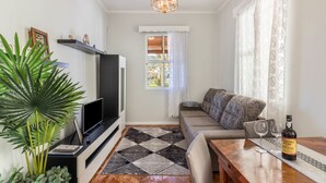 En stue med fjernsyn, sofa, spisebord og en flaske vin.