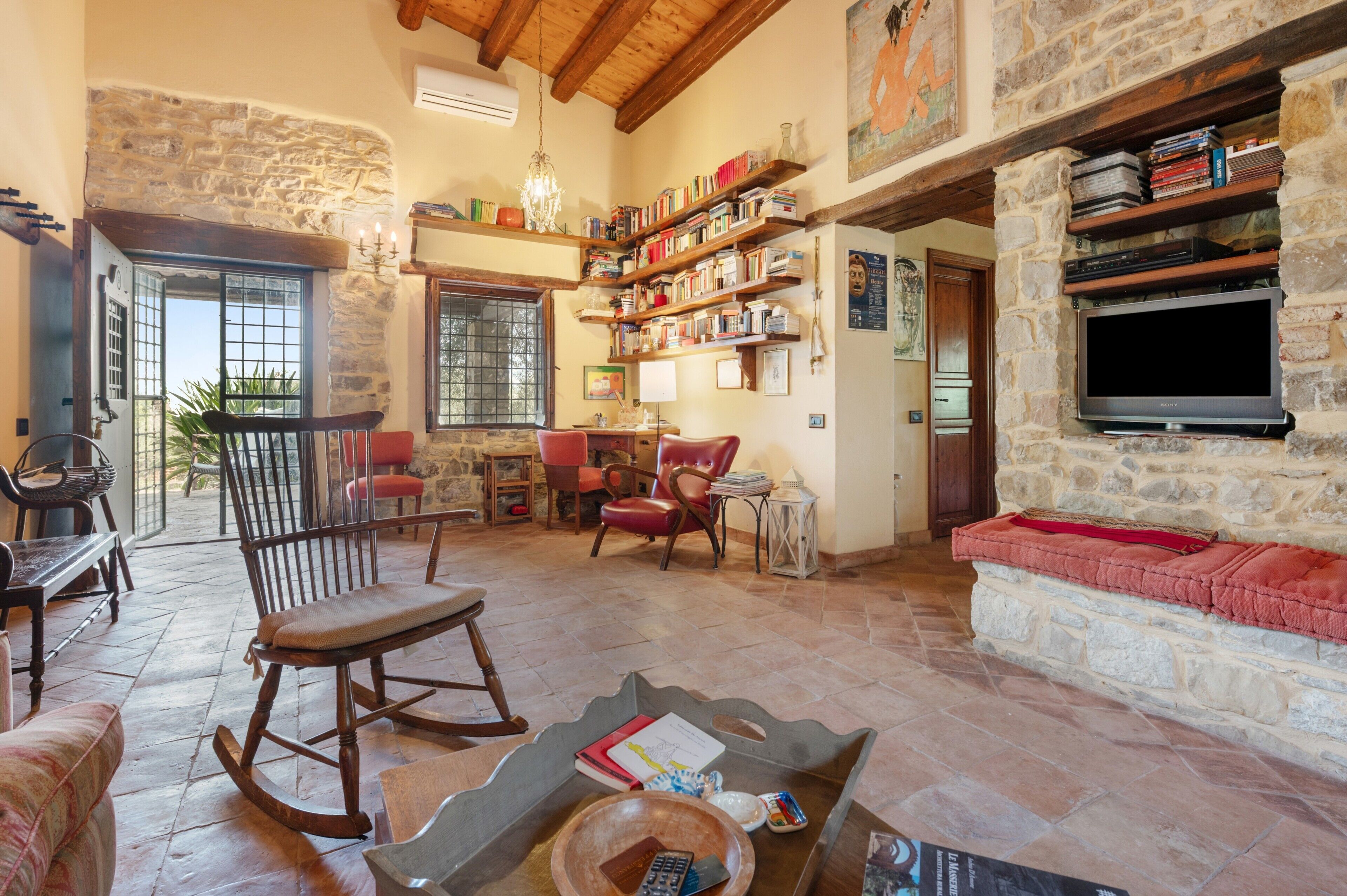 A spacious living room with a stone fireplace, wooden furniture, and a bookshelf filled with books.