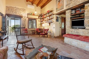 A spacious living room with a stone fireplace, wooden furniture, and a bookshelf filled with books.