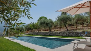 A swimming pool with a stone wall and wooden fence, surrounded by greenery and a clear sky. - Casa Degli Ulivi with sea view, Wi-Fi, and pet-friendly accommodation (Collesano)