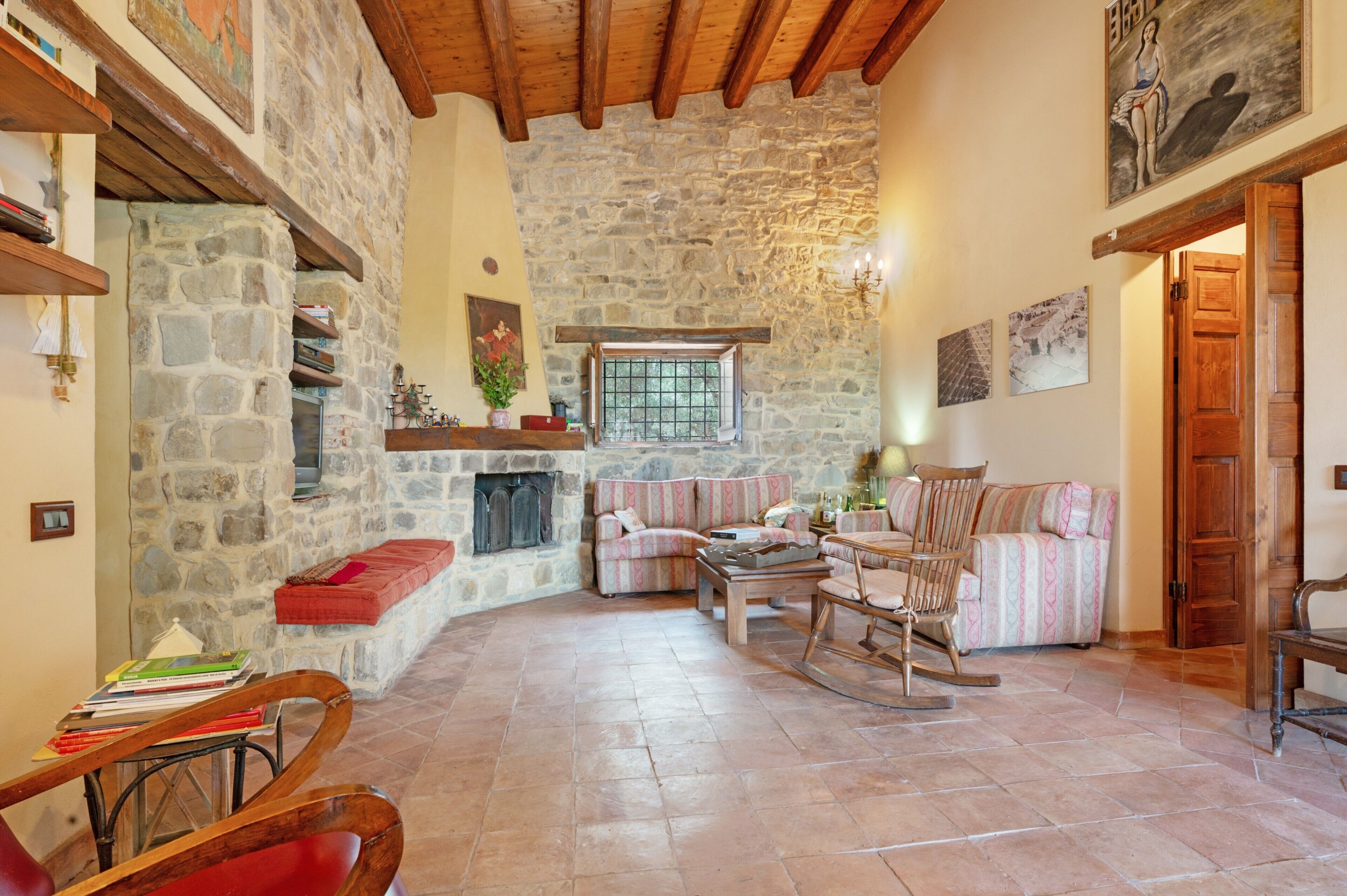 A cozy living room with stone walls, wooden beams, a fireplace, and comfortable seating.