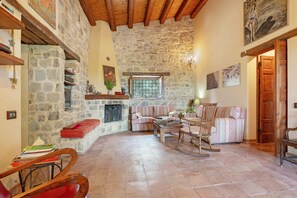 A cozy living room with stone walls, wooden beams, a fireplace, and comfortable seating.