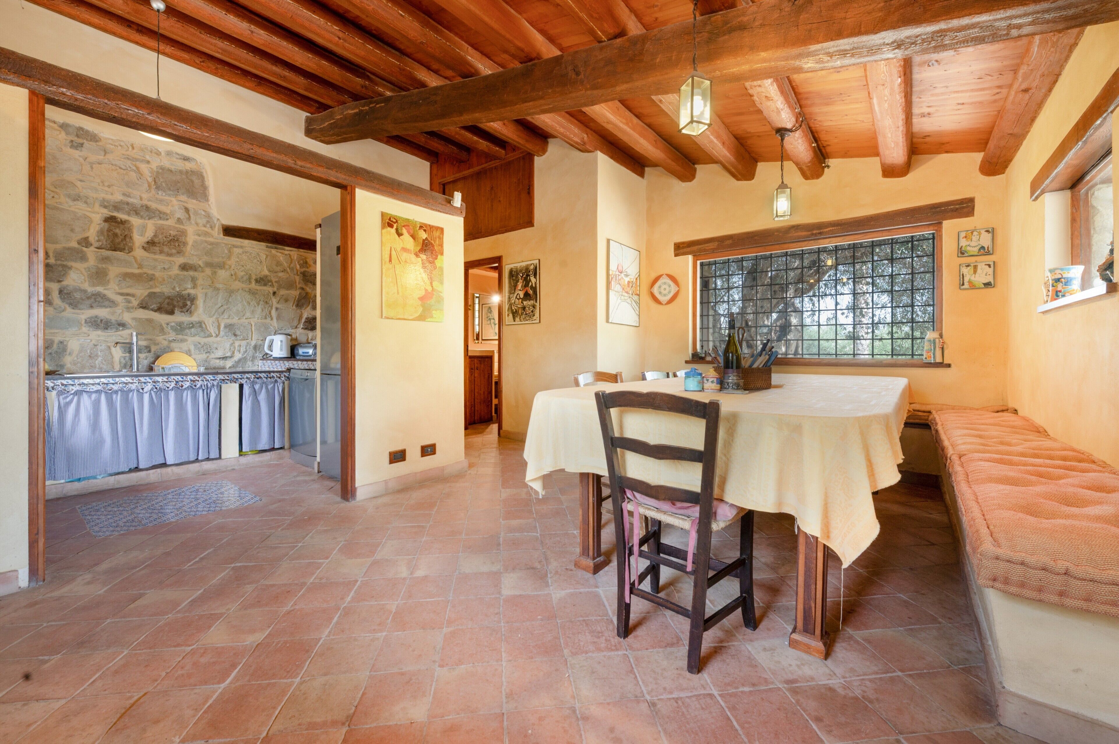 A rustic dining area with a stone wall, wooden beams, and a tiled floor.
