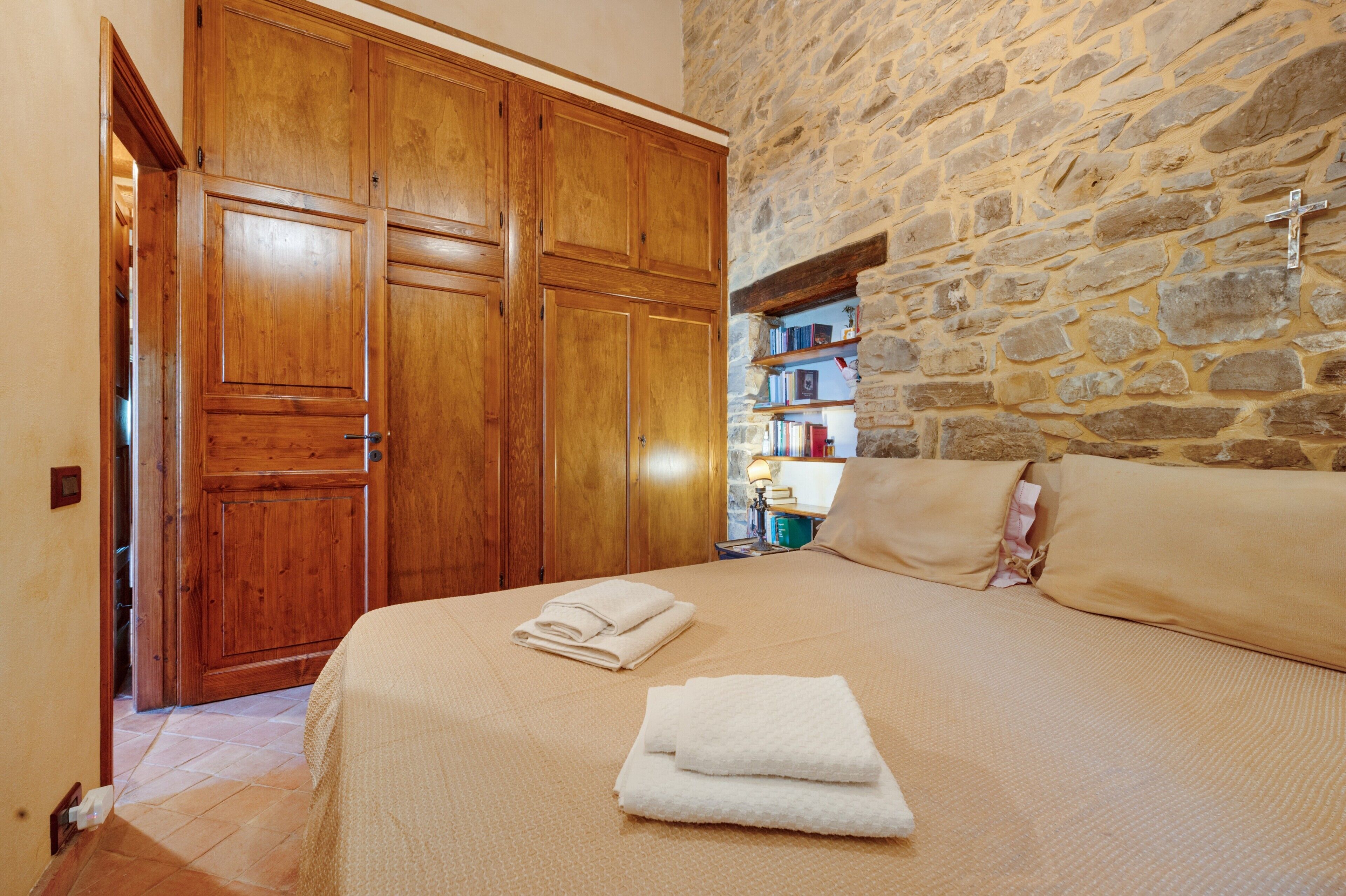 A bedroom with a stone wall, wooden wardrobe, and a bed with towels.