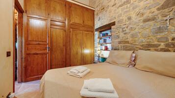 A bedroom with a stone wall, wooden wardrobe, and a bed with towels.
