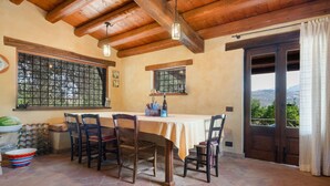 A dining area with a table set for four, wooden chairs, a window with a view, and a door leading outside. - Casa Degli Ulivi with sea view, Wi-Fi, and pet-friendly accommodation (Collesano)