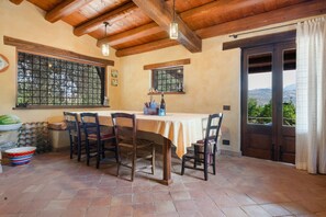 A dining area with a table set for four, wooden chairs, a window with a view, and a door leading outside. - Casa Degli Ulivi with sea view, Wi-Fi, and pet-friendly accommodation (Collesano)