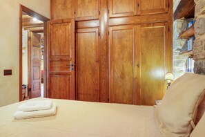 A bedroom with a bed, a wooden wardrobe, and a stone wall. - Casa Degli Ulivi with sea view, Wi-Fi, and pet-friendly accommodation (Collesano)