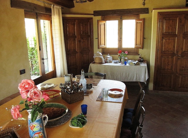 A dining area with a table set for two, a vase of flowers, and a window with curtains.