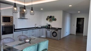 Eine moderne Küche mit integrierten Geräten, ein Essbereich mit Glastisch und eine Waschmaschine.