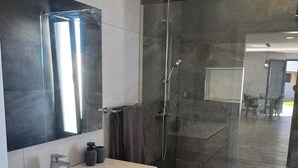 Ein modernes Badezimmer mit großem Spiegel, Waschtisch und Duschkabine, mit Blick in einen weiteren Raum.