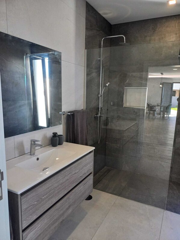 A modern bathroom with a large mirror, a vanity with a sink, a shower enclosure, and a view into another room. - An apartment with a view of the sea, equipped with all the amenities you need for a relaxing vacation (Arco da Calheta)