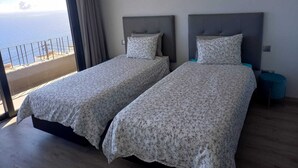 Ein Zimmer mit zwei Betten, einem großen Fenster mit Meerblick und einer Klimaanlage an der Wand.