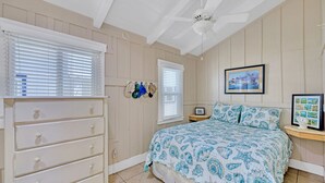 Un dormitorio con cama, cómoda, ventilador de techo y una obra de arte colgada en la pared.