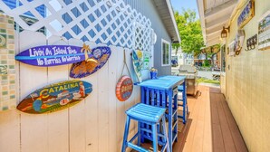 Un patio con un muro blanco de celosía, taburetes azules y varios carteles, incluyendo uno que dice "Livin' On Island Time No Harris No Worries".