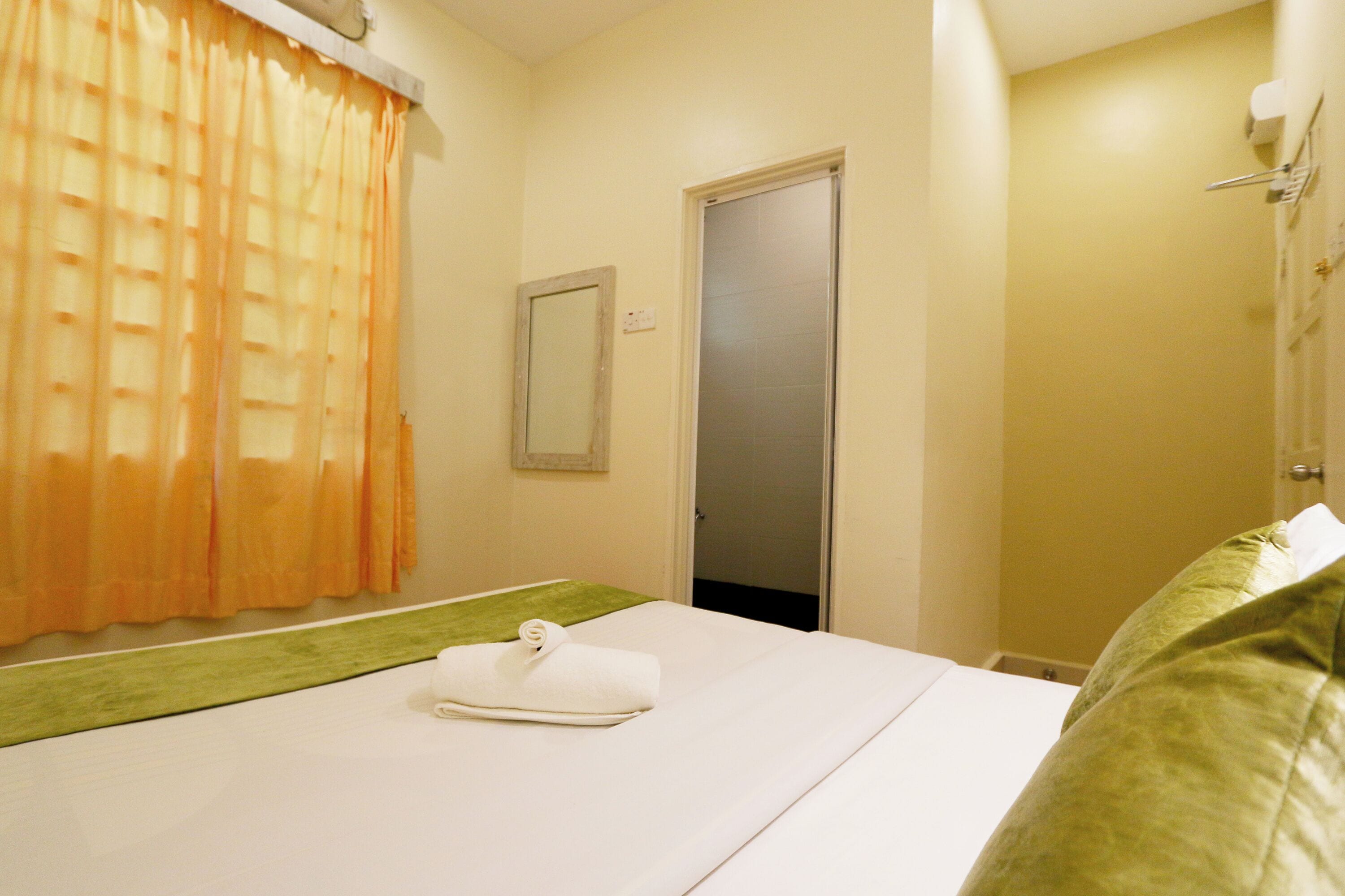 A hotel room with a bed, a bathroom door, and a shower area.