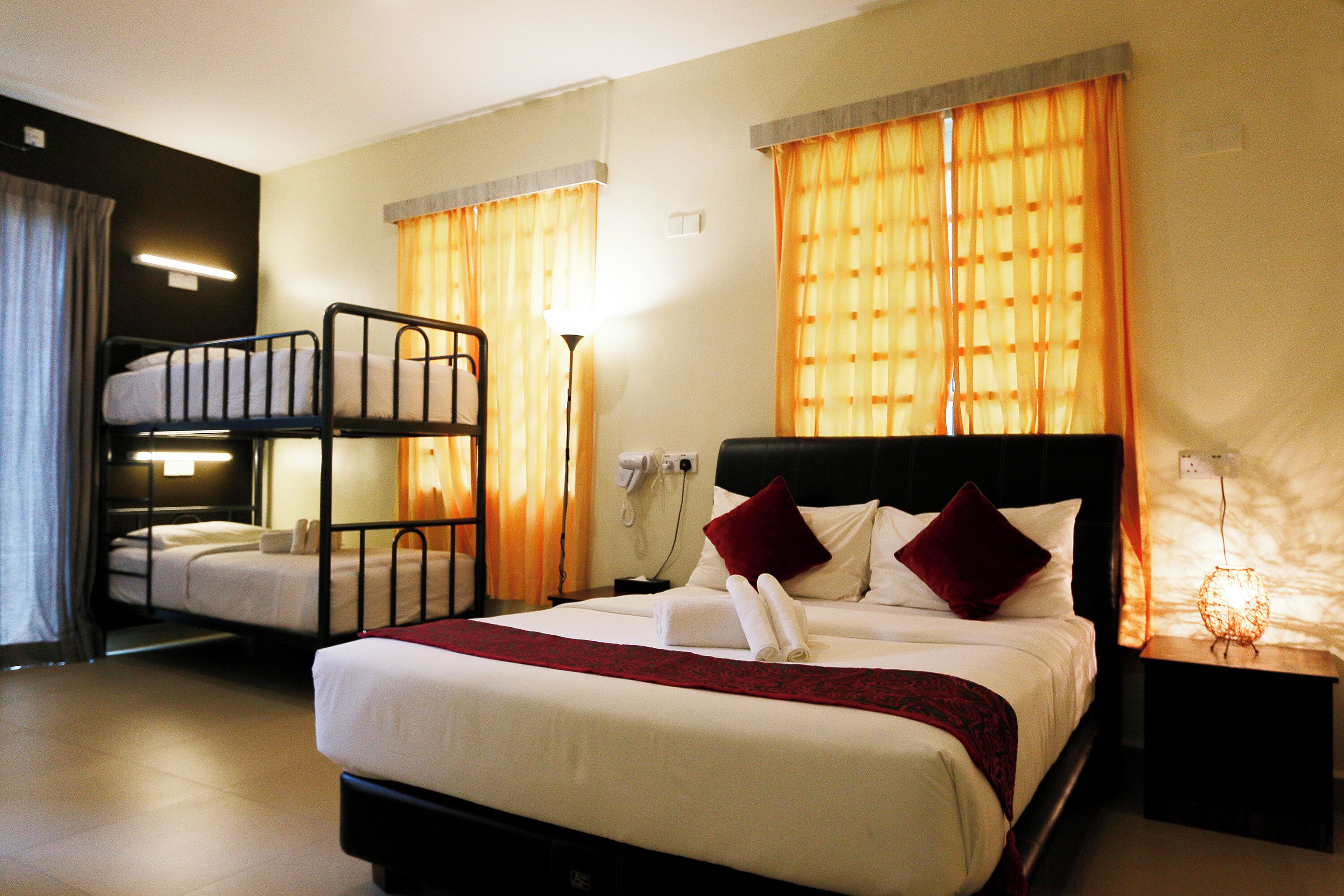 Una camera d'albergo con un letto matrimoniale, un letto a castello più piccolo, una lampada da comodino e un comodino.