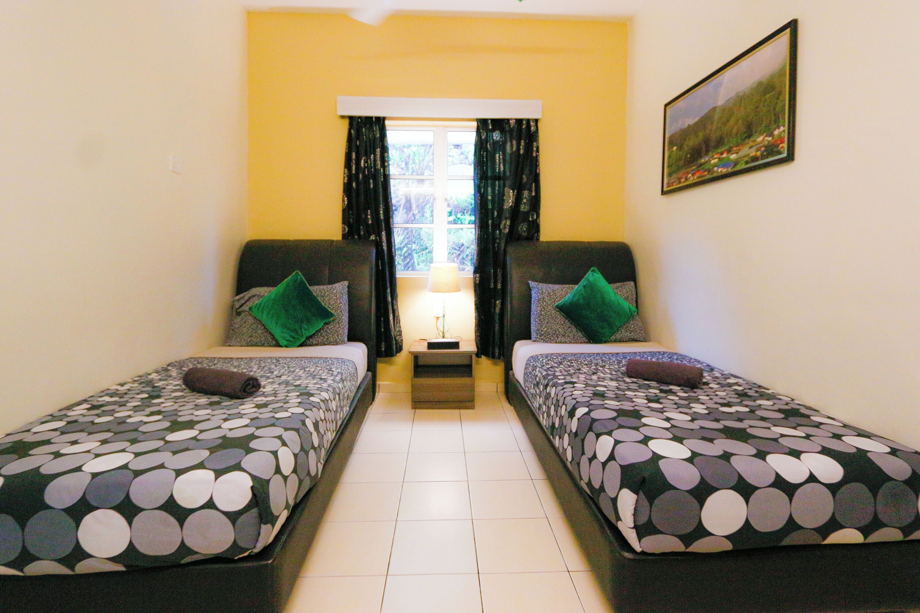 A room with two beds, each with a patterned bedspread, a small bedside table with a lamp, and a window with curtains.