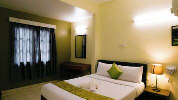 A hotel room with a large bed, a bedside table with a lamp, a desk, and a window with curtains.