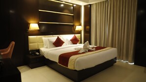 Una habitación de hotel con una cama grande, una mesita de noche, una silla y un ventanal con cortinas.