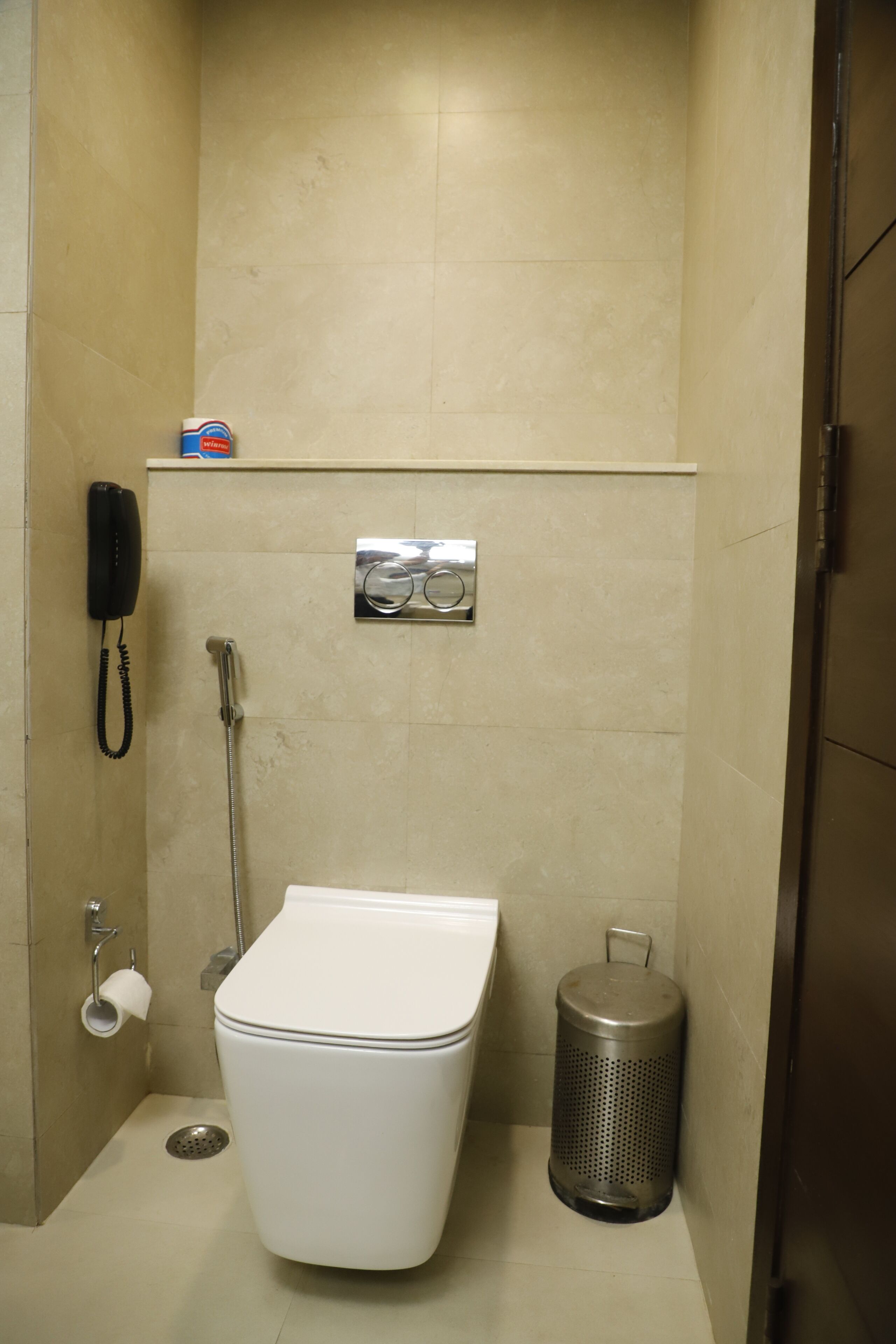 Baño con inodoro, cubo de basura, secador de manos y teléfono.