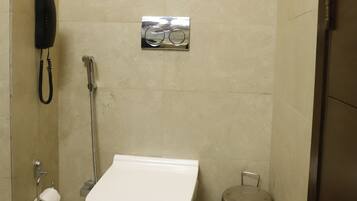 Baño con inodoro, cubo de basura, secador de manos y teléfono.