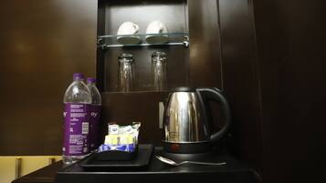 Una cafetera con una botella de agua, cápsulas de café y un portavasos con tazas.