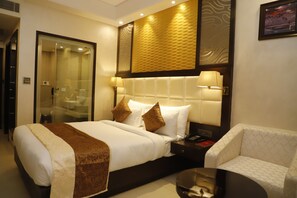 A hotel room with a large bed, a bedside table with a lamp, a glass-enclosed shower, and a small sofa. - Udman By Ferns N Petals, Chattarpur (New Delhi)