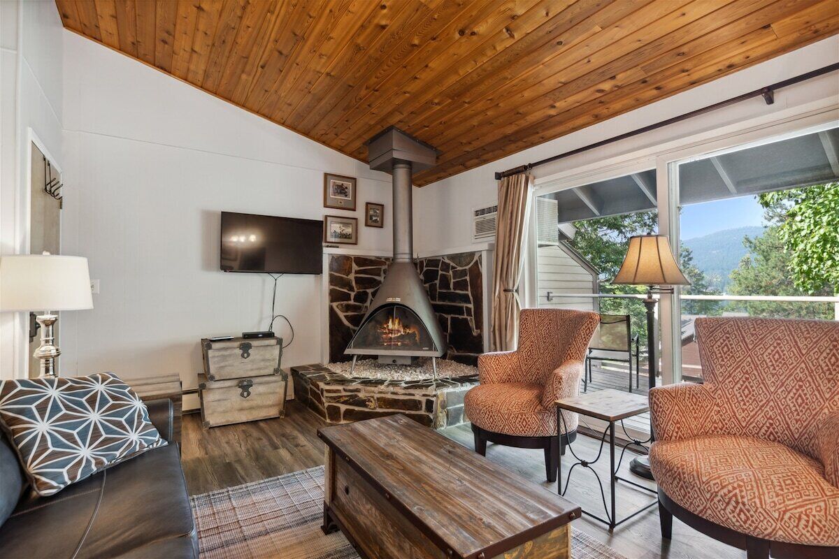 A cozy living room with a stone fireplace, leather furniture, and a TV mounted on the wall.