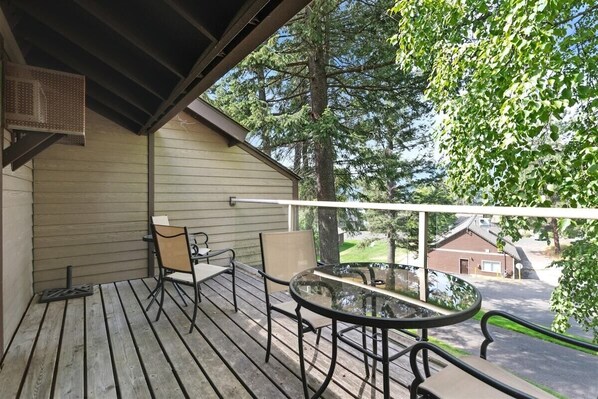 A covered outdoor area with a table and chairs, a view of a street, and a building in the background. - Whitefish Lake Condo, 14BU, hillside! (Whitefish)