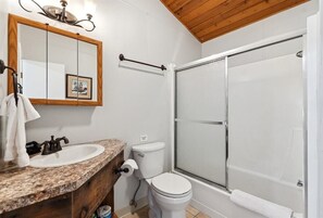 A bathroom with a wooden vanity, a sink, a toilet, and a glass-enclosed shower. - Whitefish Lake Condo, 14BU, hillside! (Whitefish)