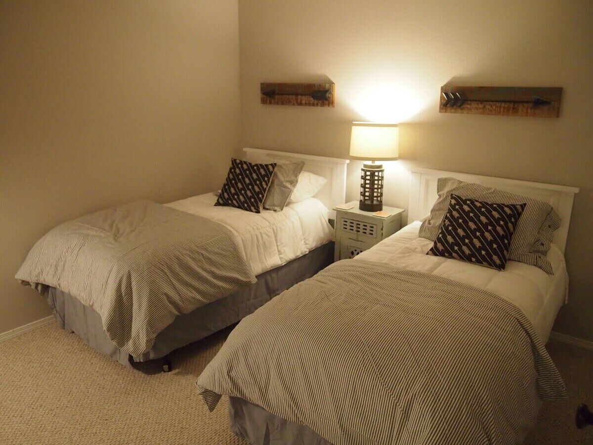 A bedroom with two beds, a nightstand with a lamp, and wall-mounted storage.