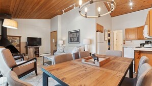 Uma sala de estar moderna com uma mesa de jantar de madeira, sofás, televisão e área de cozinha.