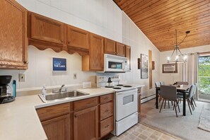 A kitchen with wooden cabinets, a white countertop, a stove, and a dining area with a table and chairs.