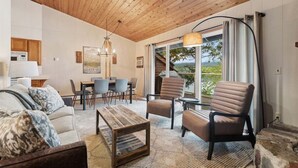Sala de estar com teto de madeira, área de jantar e vista para o verde lá fora.