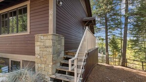 Una cabaña de madera con escalones y pared de piedra, rodeada de árboles.