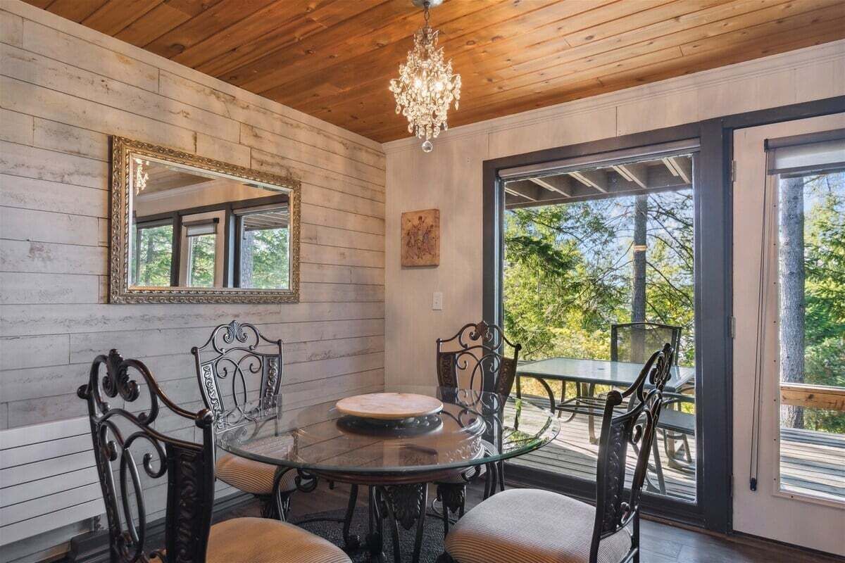 A dining area with a round glass table, metal chairs, a chandelier, a large mirror, and a view of the outdoors.