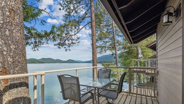 Une terrasse dotée d’une table et de chaises en verre, offrant une vue sur un lac et des montagnes au loin.
