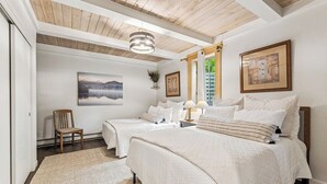 Une chambre avec deux lits, un plafond en bois, un tableau et une fenêtre avec des rideaux.