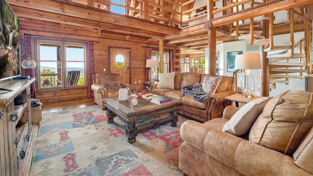 A log cabin interior with a large window, a fireplace, a sofa, and a coffee table. - Sequoyah Lodge - 1.5 mi to DT (Fayetteville)
