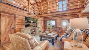 A log cabin interior with a cozy living area featuring leather furniture, a television, and a rustic wooden ceiling. - Sequoyah Lodge - 1.5 mi to DT (Fayetteville)